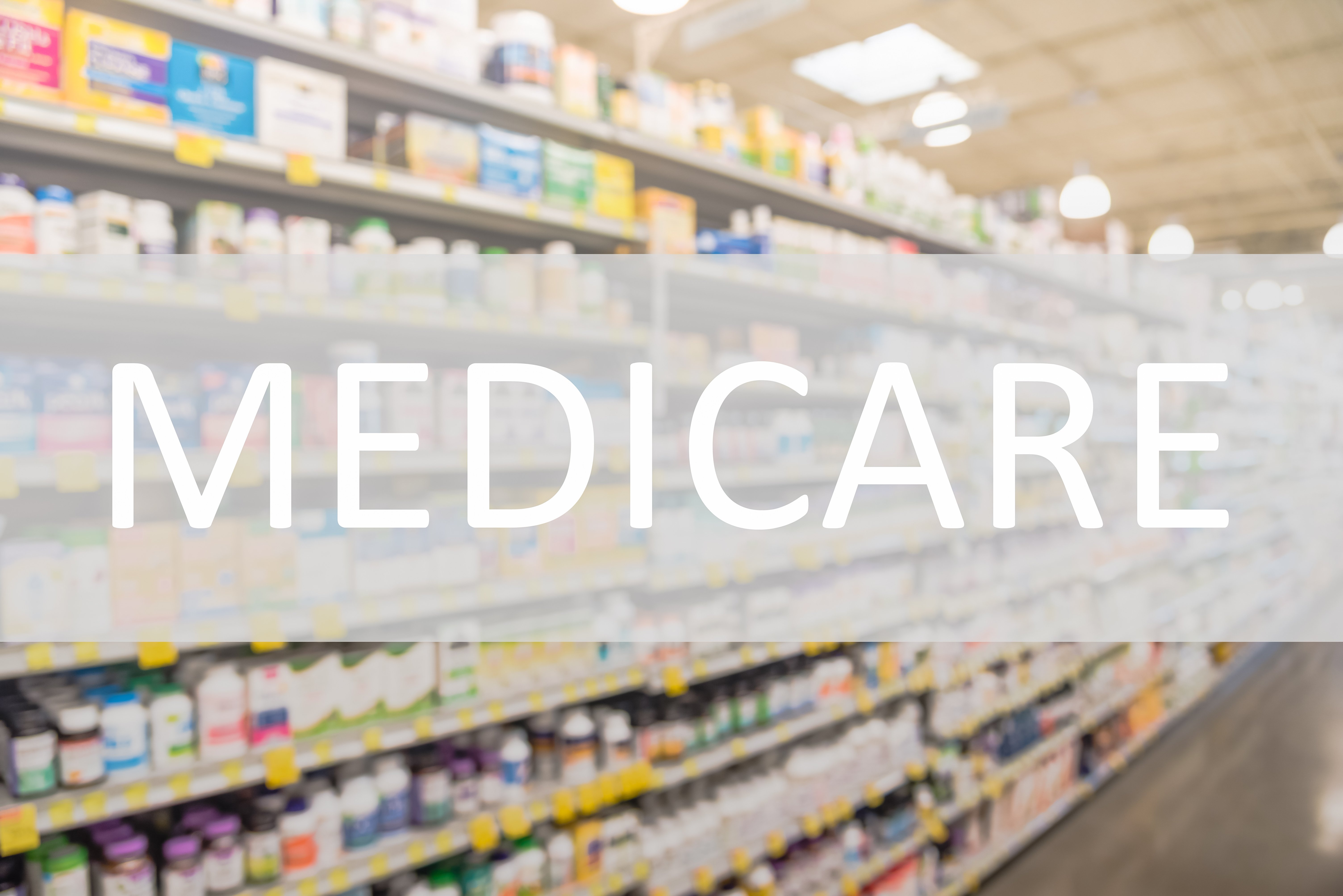Blurred pharmacy aisle with shelves of medications and the word ‘Medicare’ overlaid across the image